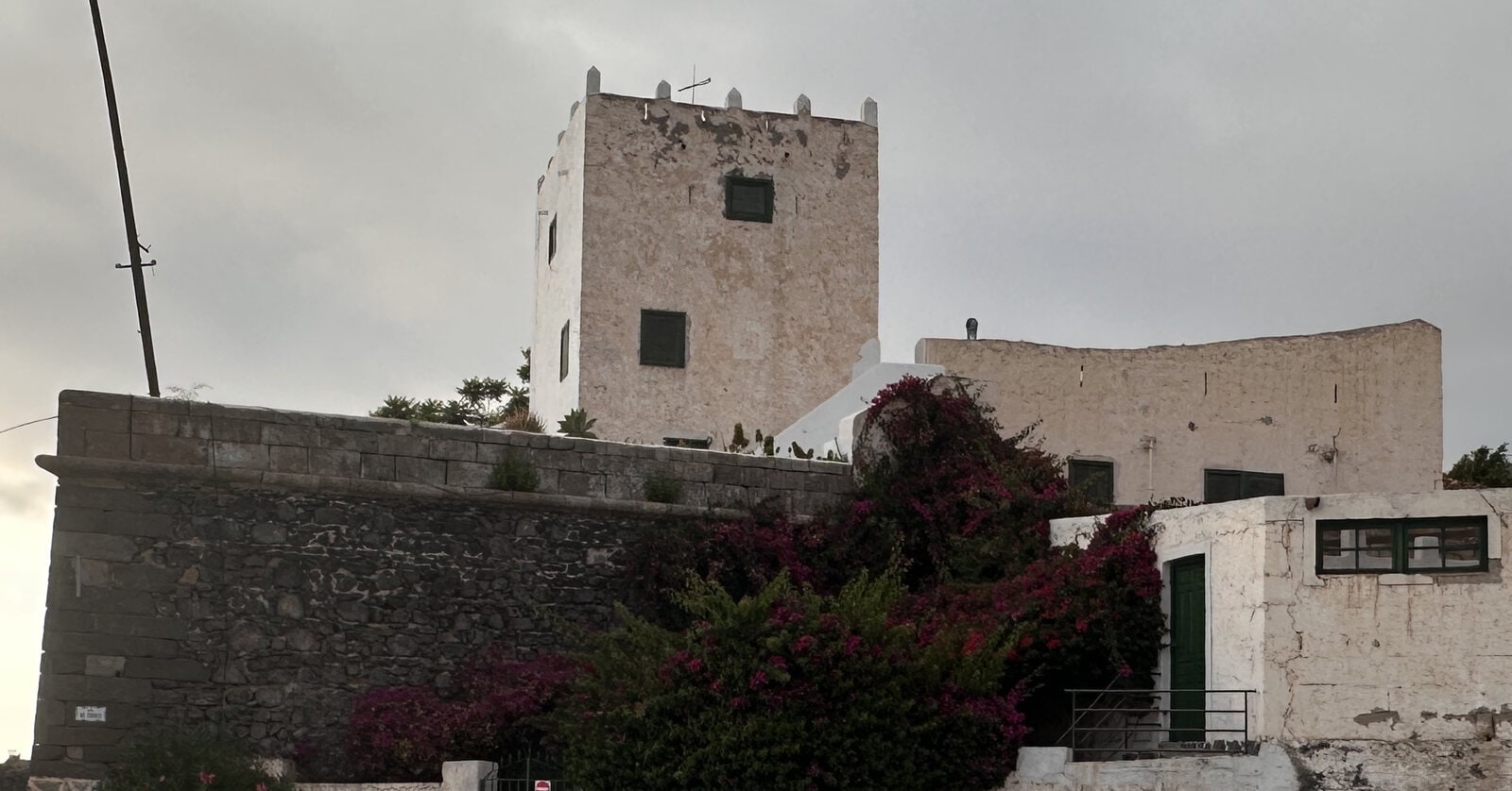 La torre almenada de la Casa Fuerte de Adeje sobre el muro defensivo de piedra volcánica, con una buganvilla en flor
