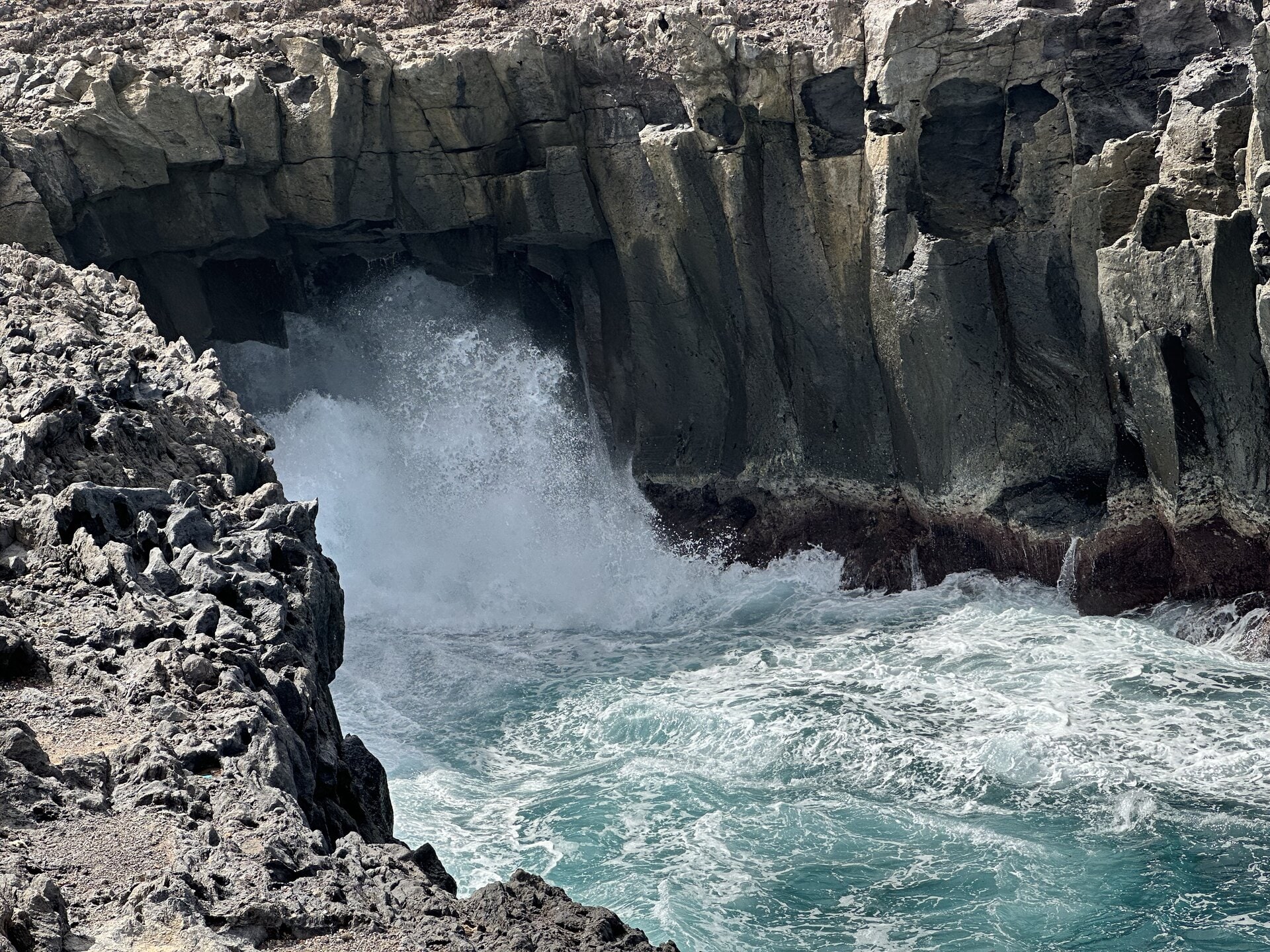 Una ola rompe dentro del bufadero de Los Silos durante un temporal de mar, con la espuma subiendo por las paredes de lava del arco.