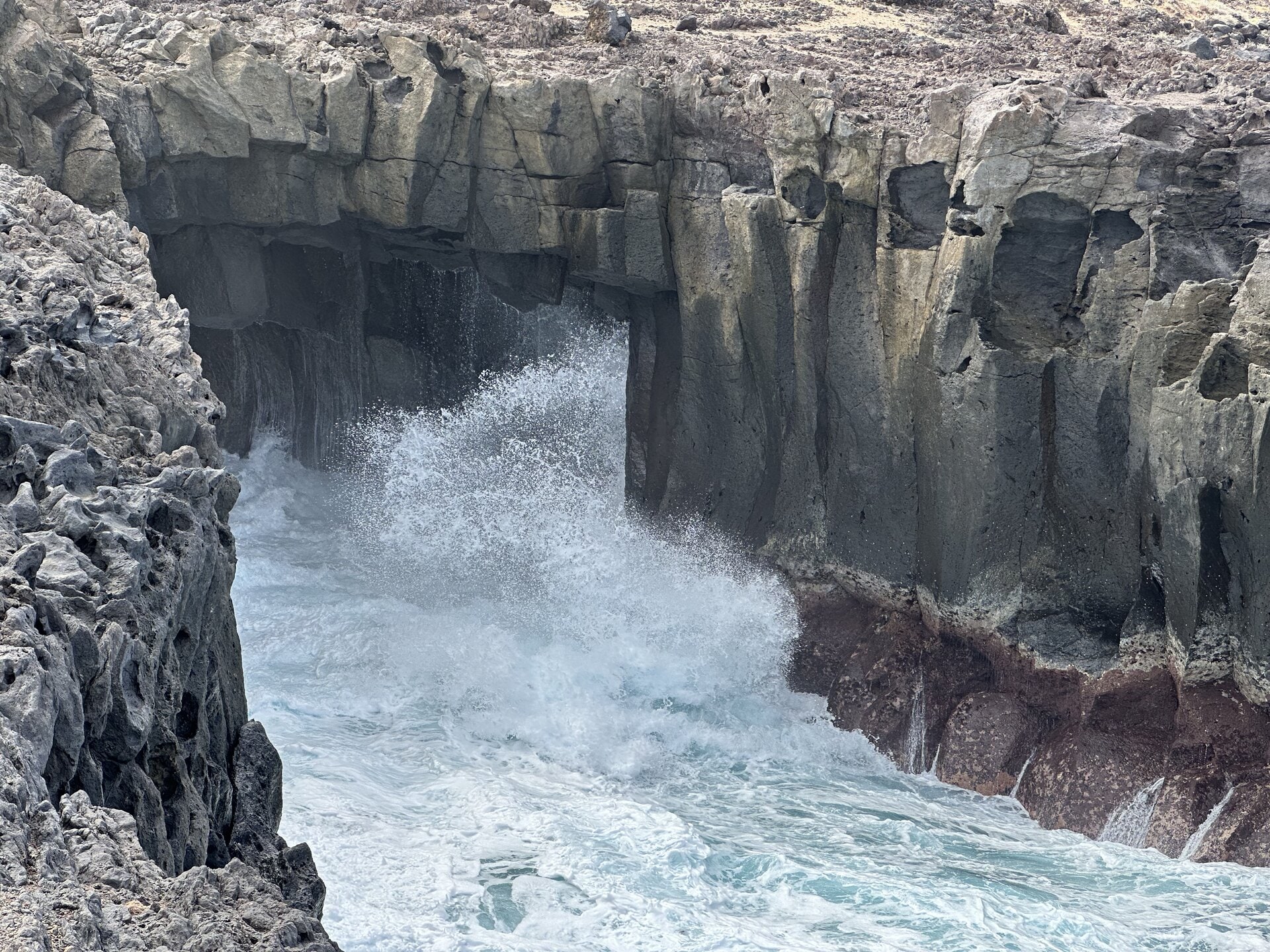 El agua entra con fuerza en la cueva marina de El Bufadero y estalla contra la roca roja del fondo, un día de oleaje fuerte en la costa de Los Silos.