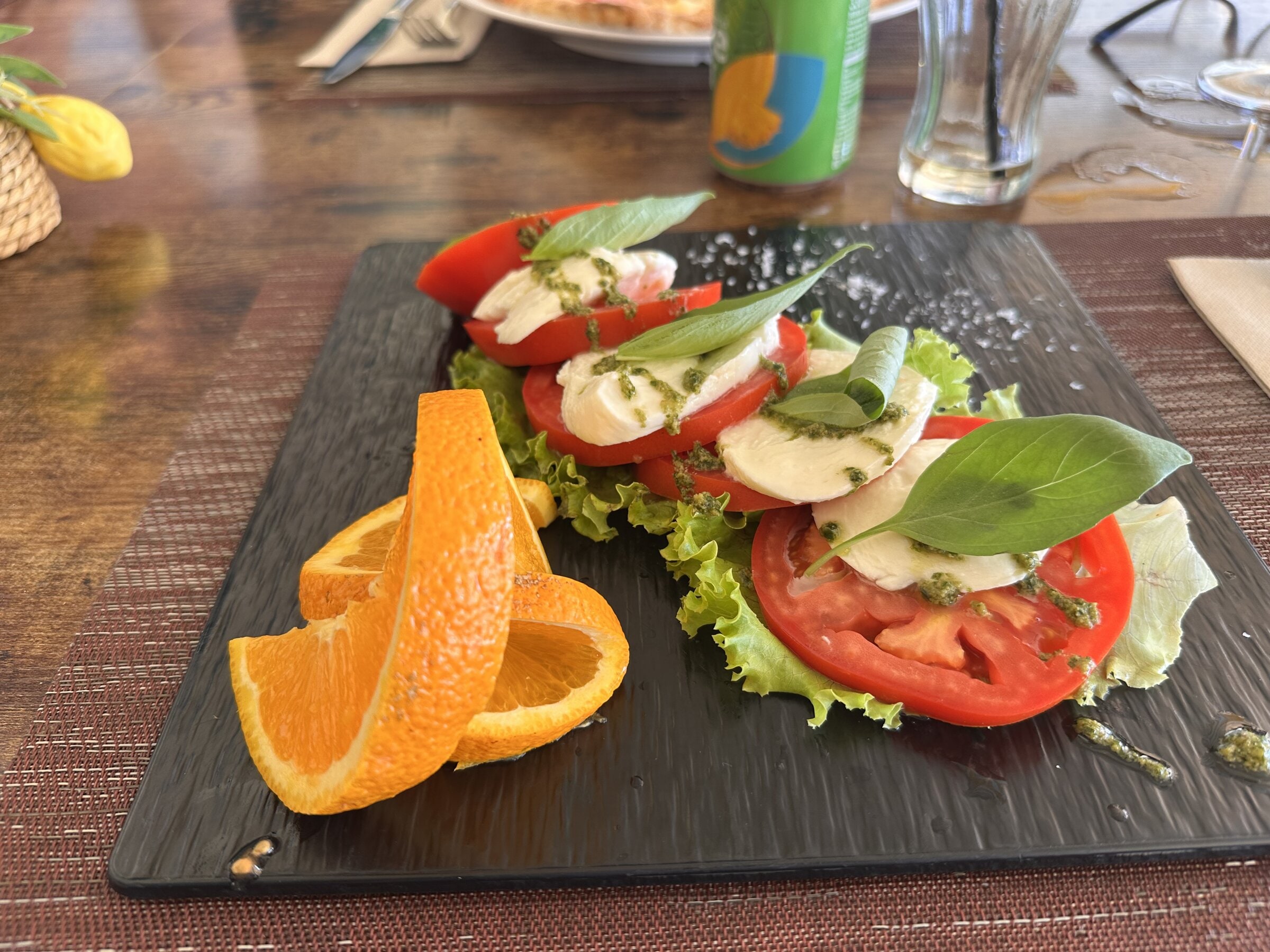 Ensalada caprese con tomate, mozzarella, albahaca y pesto, servida sobre pizarra negra con rodajas de naranja en el restaurante Limoncello de Costa Adeje.
