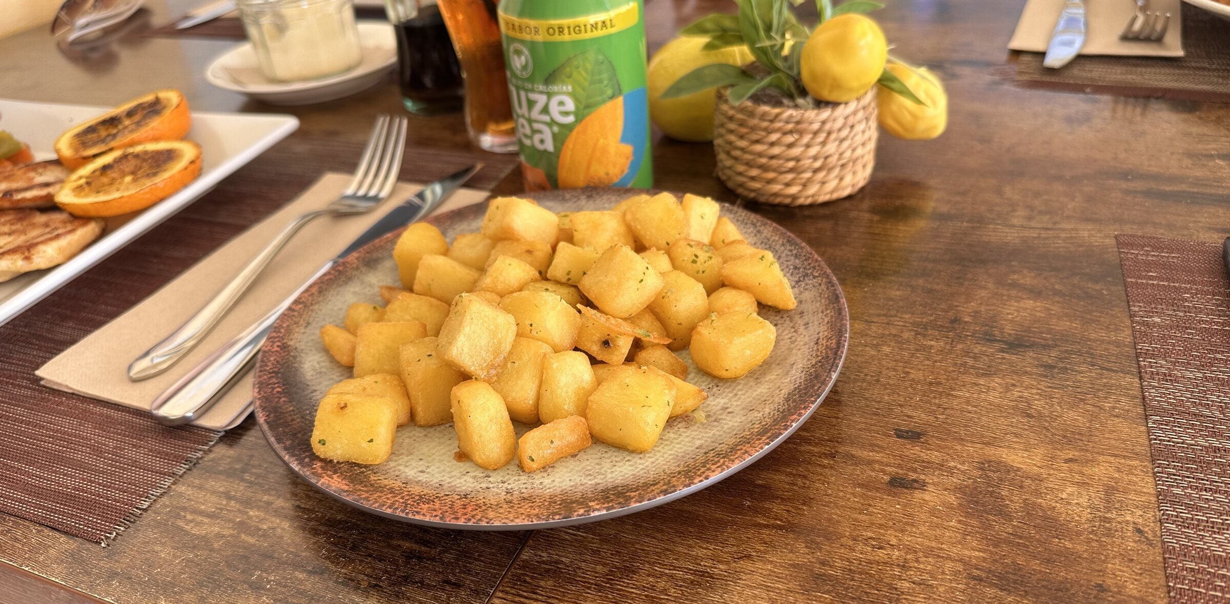 Plato de patatas salteadas en dados sobre una mesa de madera, con una maceta de limones decorativos al fondo, en el restaurante Limoncello.