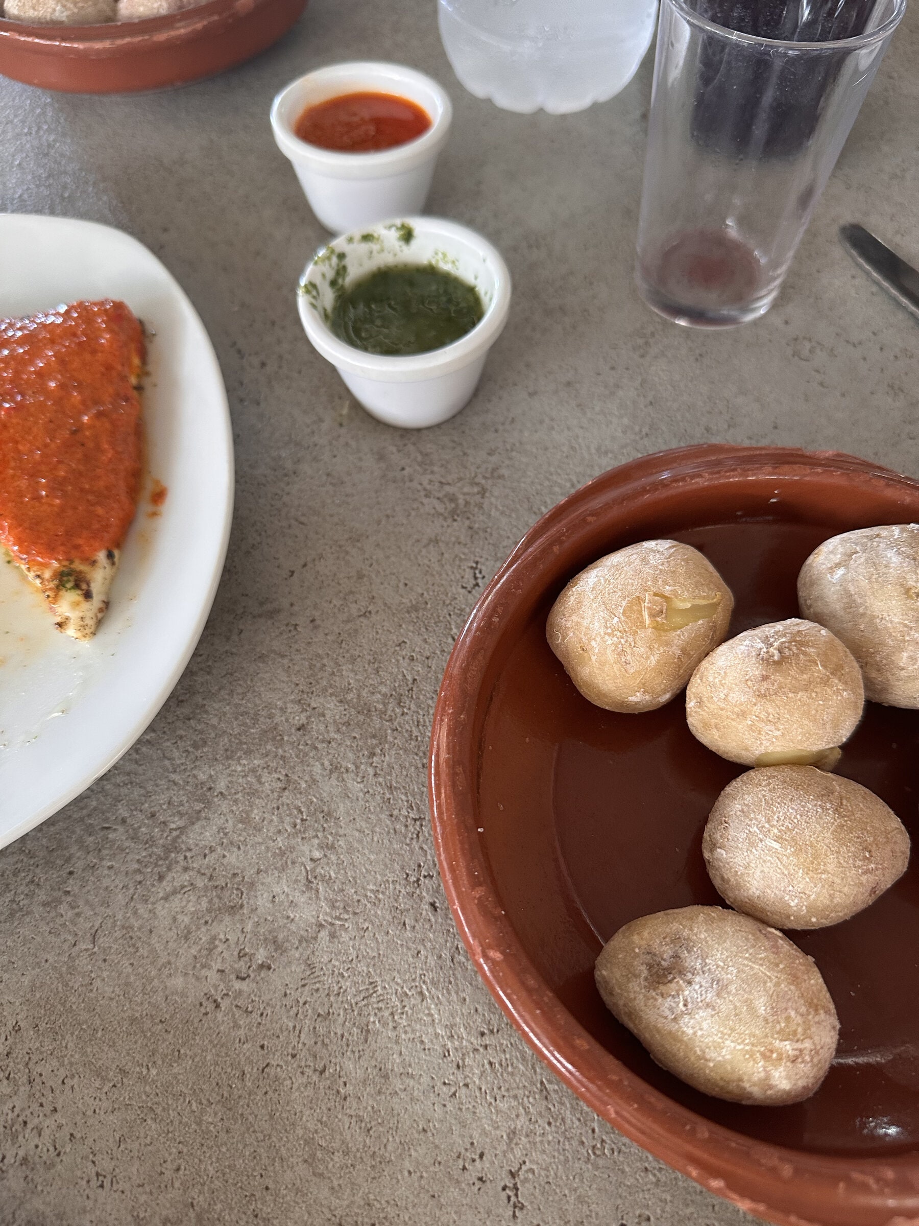Papas arrugadas en cazuela de barro con mojo rojo y mojo verde; al lado, queso con mojo rojo.