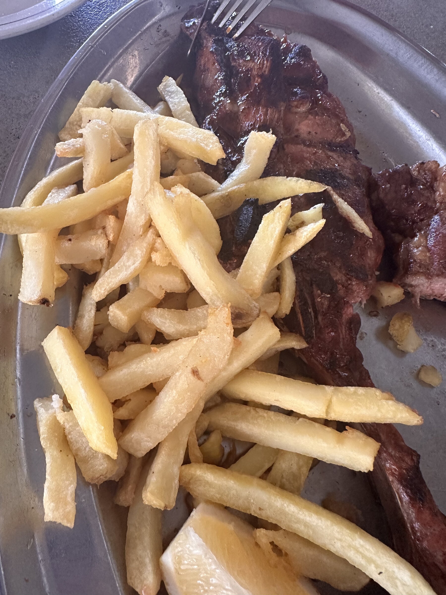 Carne asada con papas fritas en una bandeja metálica.