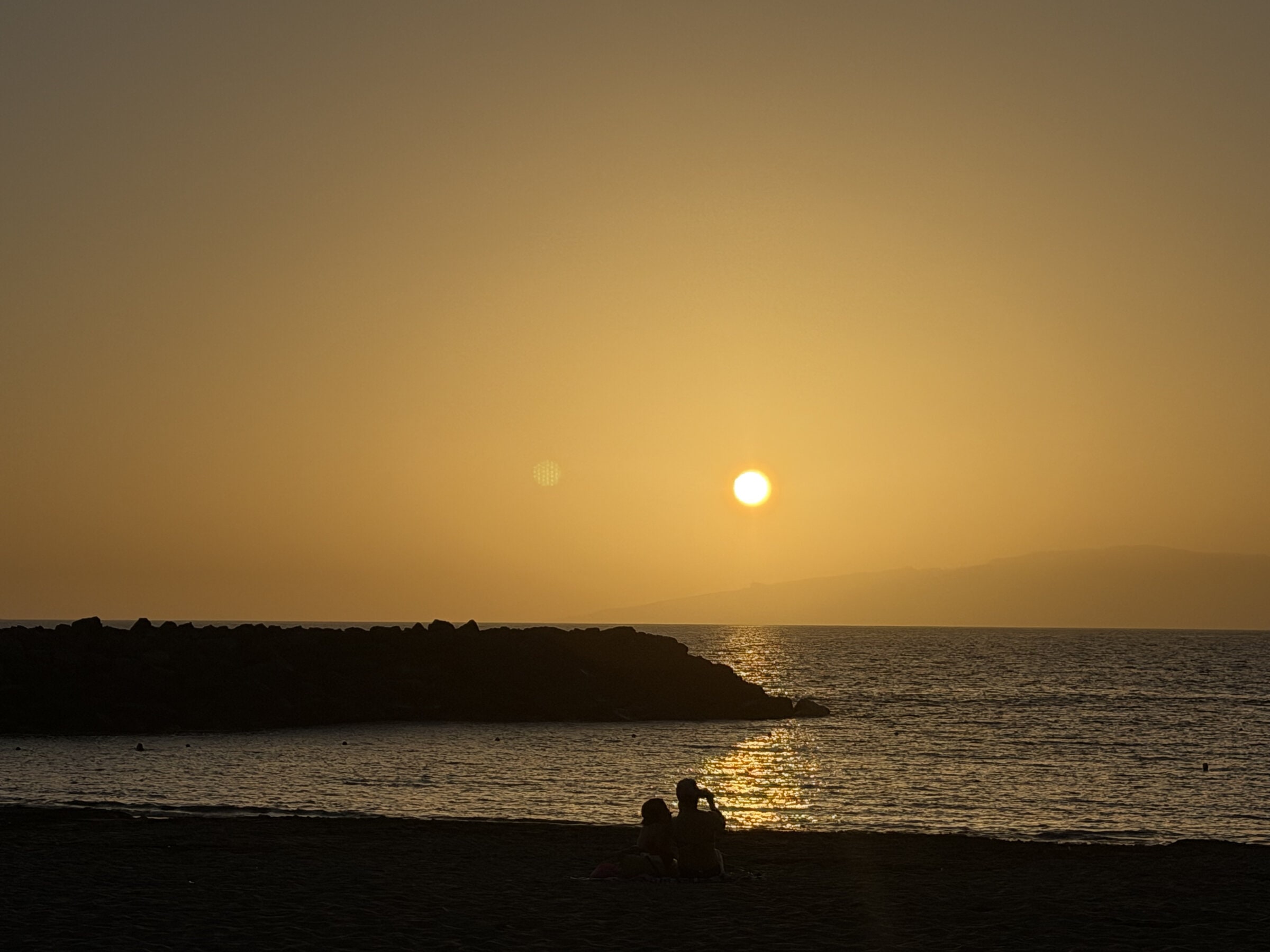 Puesta de sol sobre el mar desde la Playa de Torviscas, con la escollera de roca y el reflejo dorado en el agua.